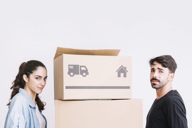 A young couple carrying moving boxes in the concept of 'Changing Address and Updating Utilities After Moving to Coulsdon'.